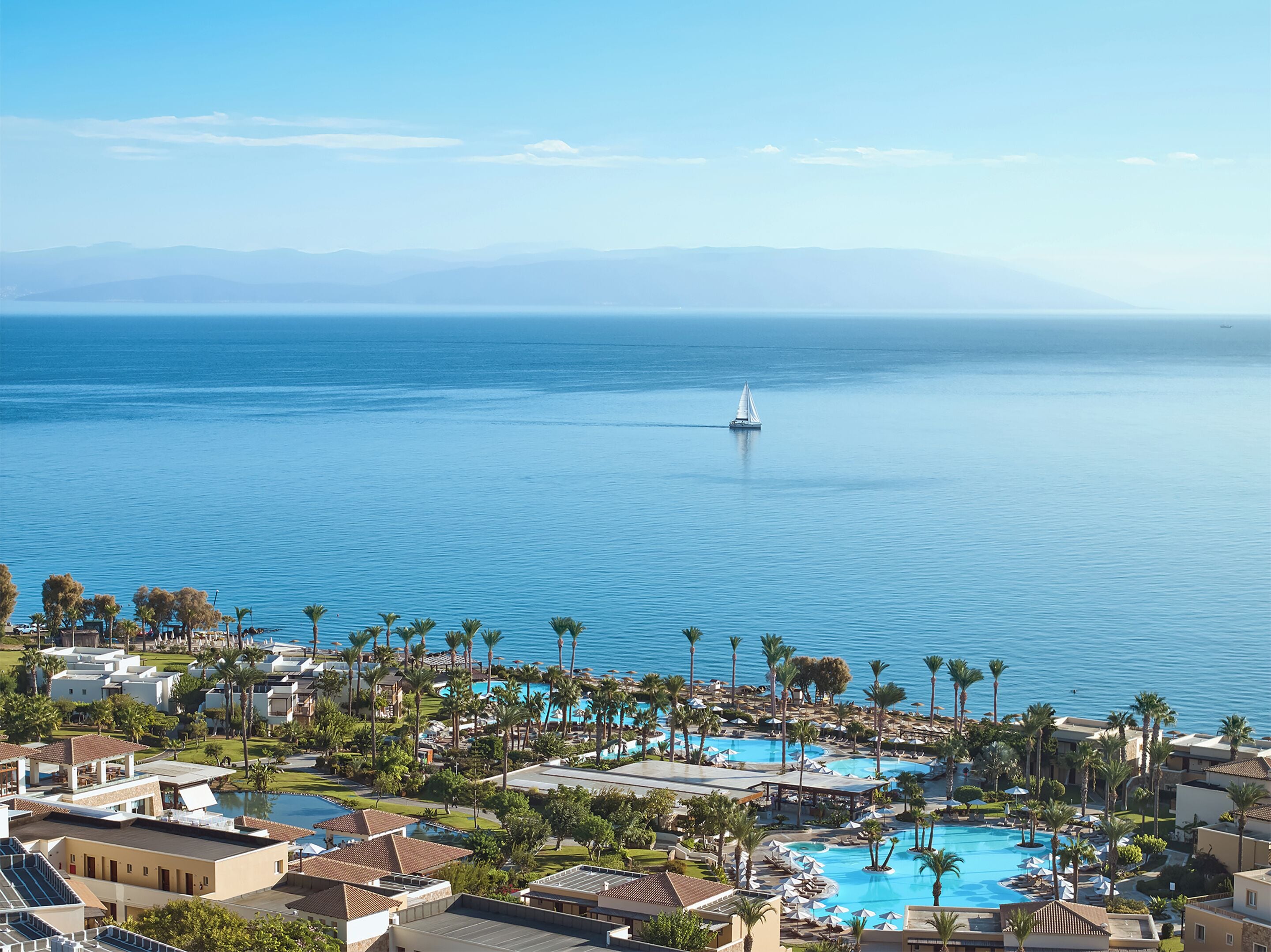 Un resort con diverse piscine, palme e un veliero sull'acqua.