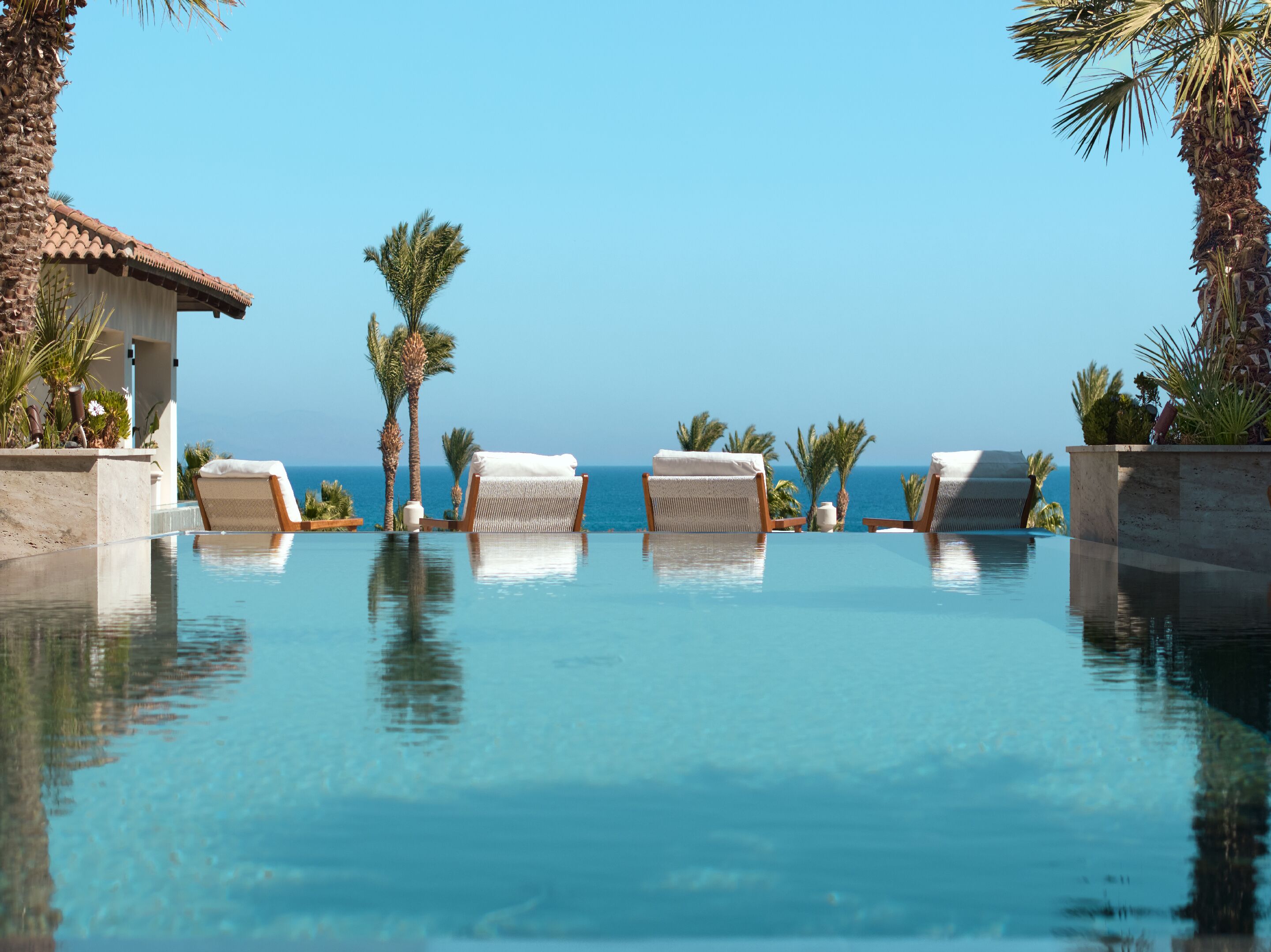 Ein Poolbereich mit Liegestühlen und Palmen, mit Blick auf das klare, blaue Meer.