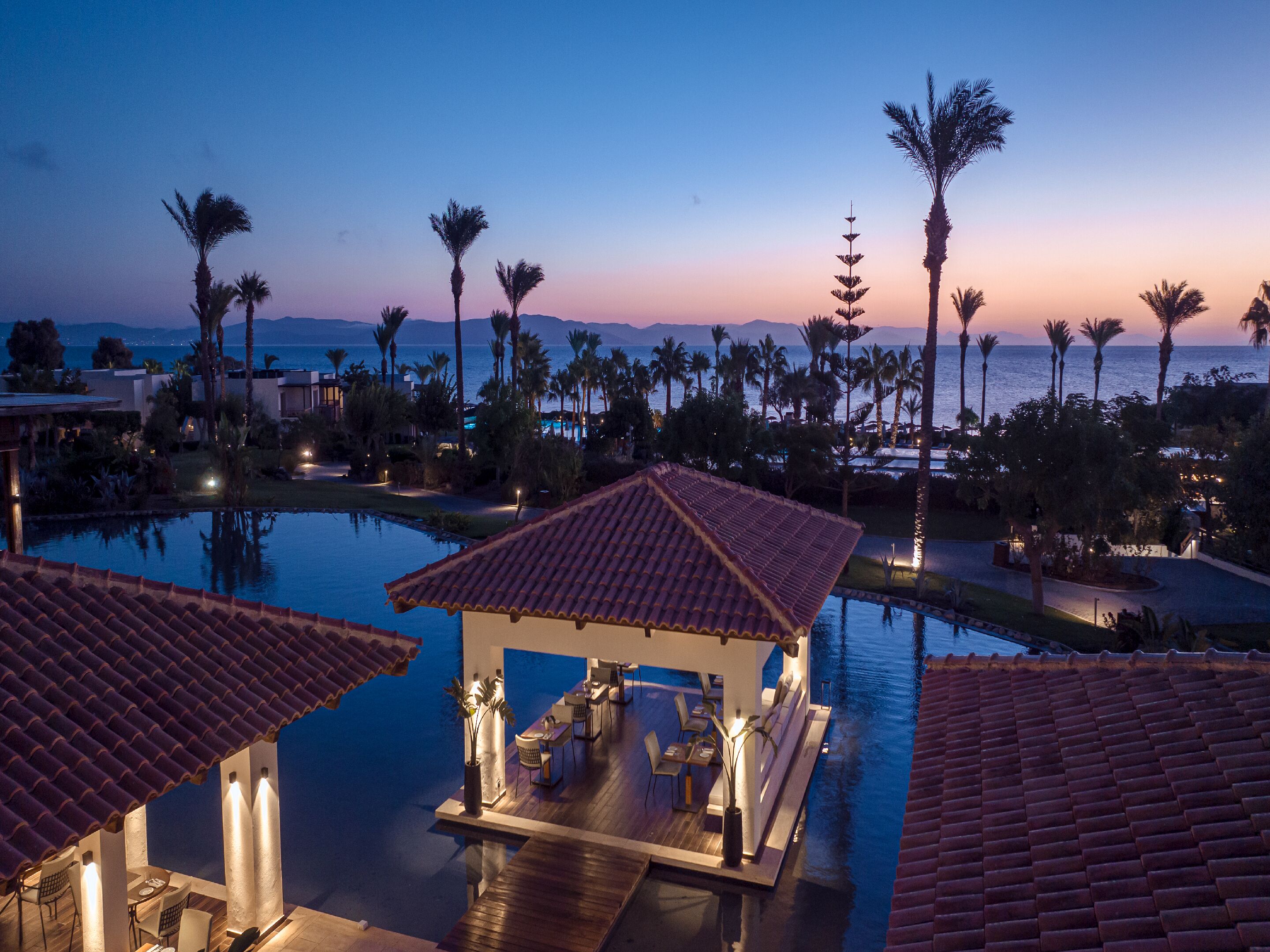 Un resort con piscina, palmeras y vista al océano al anochecer.