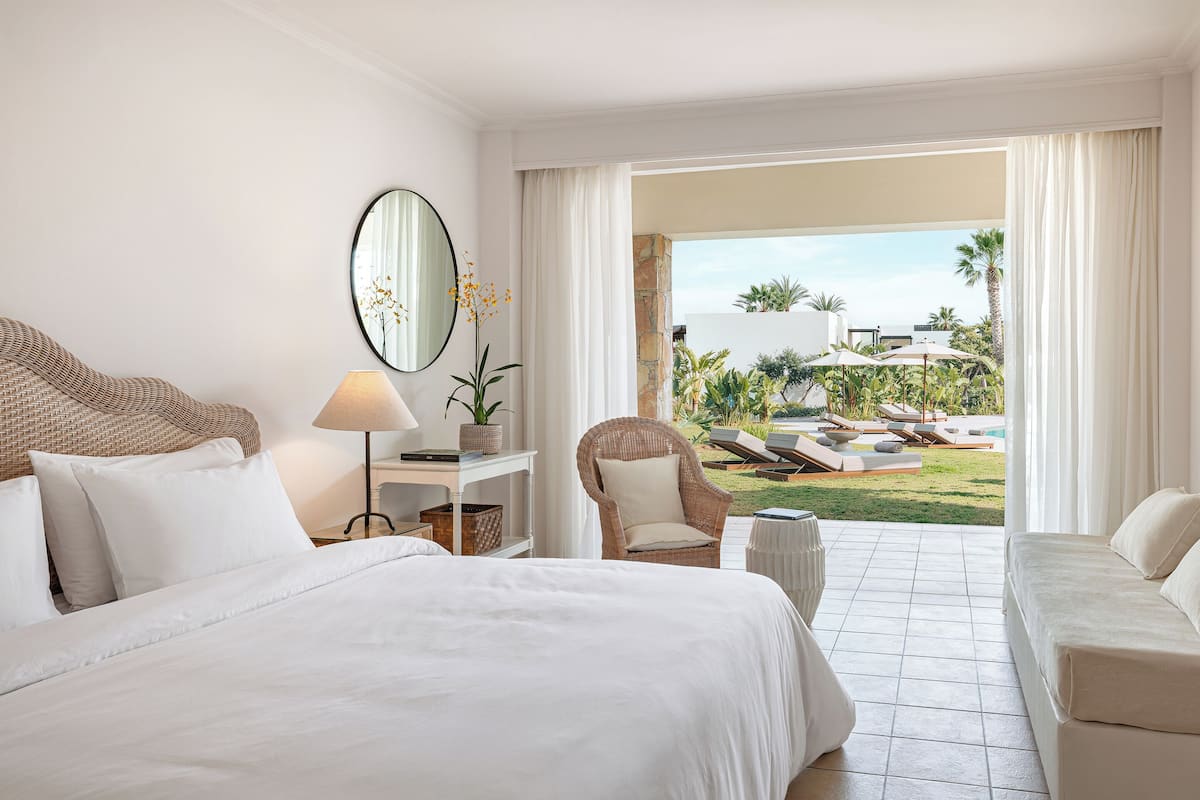 Une chambre d’hôtel avec un grand lit, un bureau, une chaise et une vue sur une piscine et un jardin.