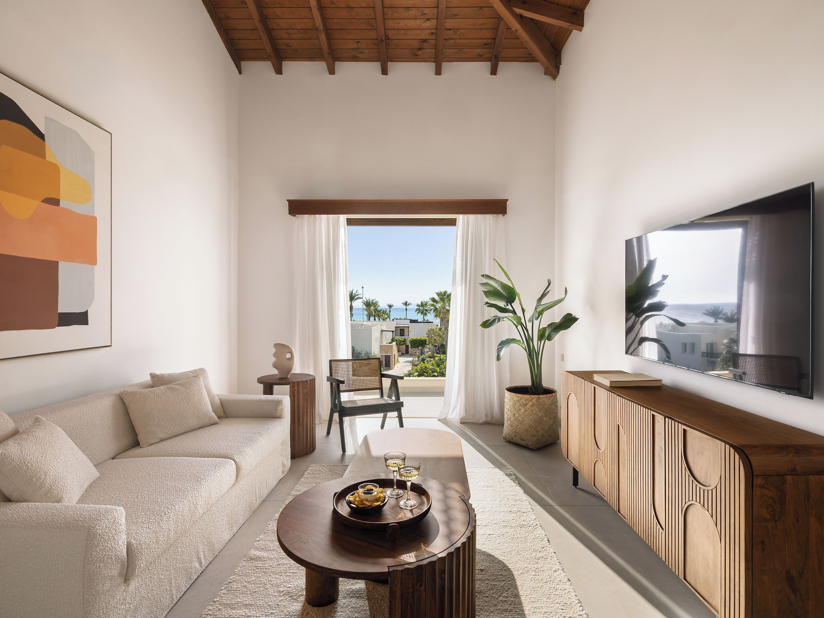 A living room with a sofa, coffee table, TV, and a balcony with a view.