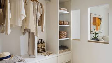 A walk-in closet with hanging clothes, shelves with baskets, a bench with shoes, and a framed picture on the wall.