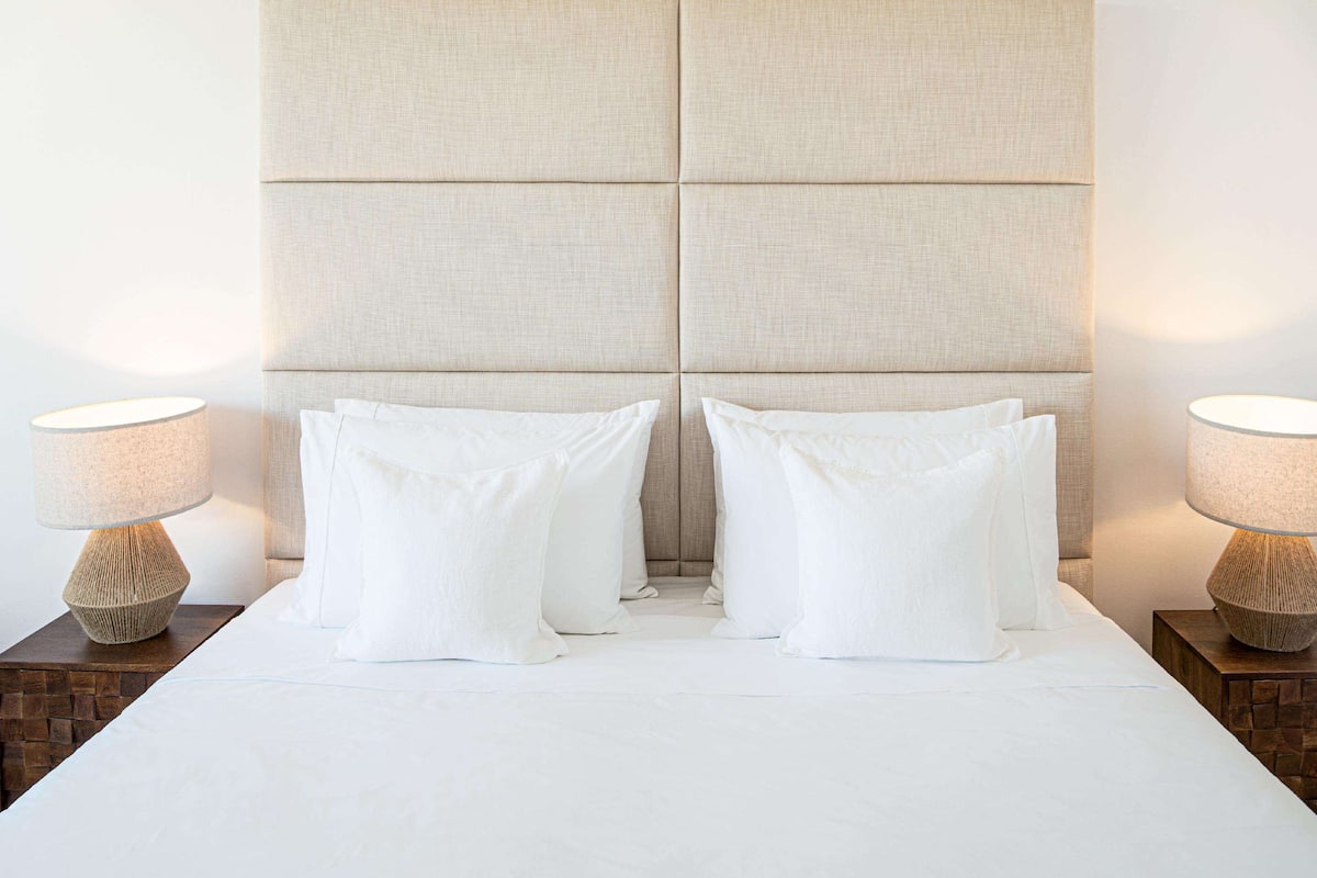 Een bed met hoofdeinde, twee nachtkastjes en twee lampen.