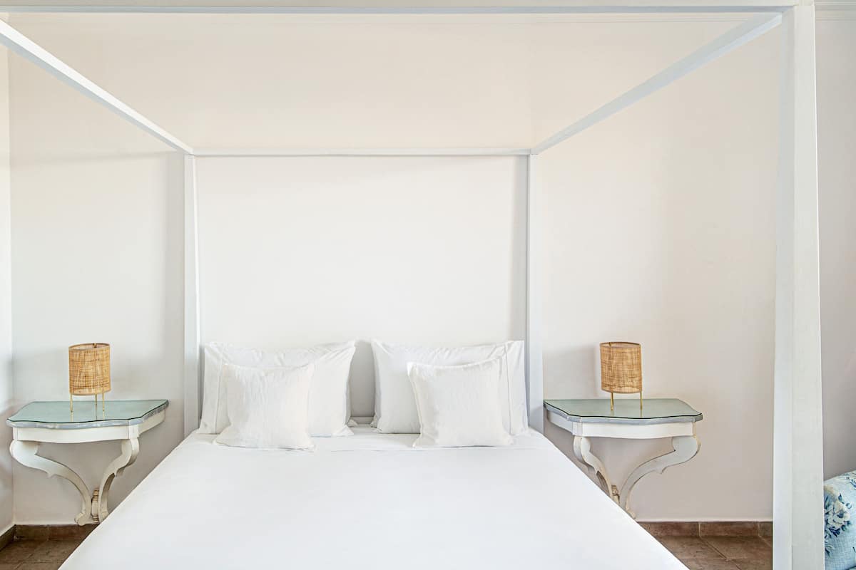 Een minimalistische slaapkamer met een groot bed, twee nachtkastjes en een effen wit plafond.