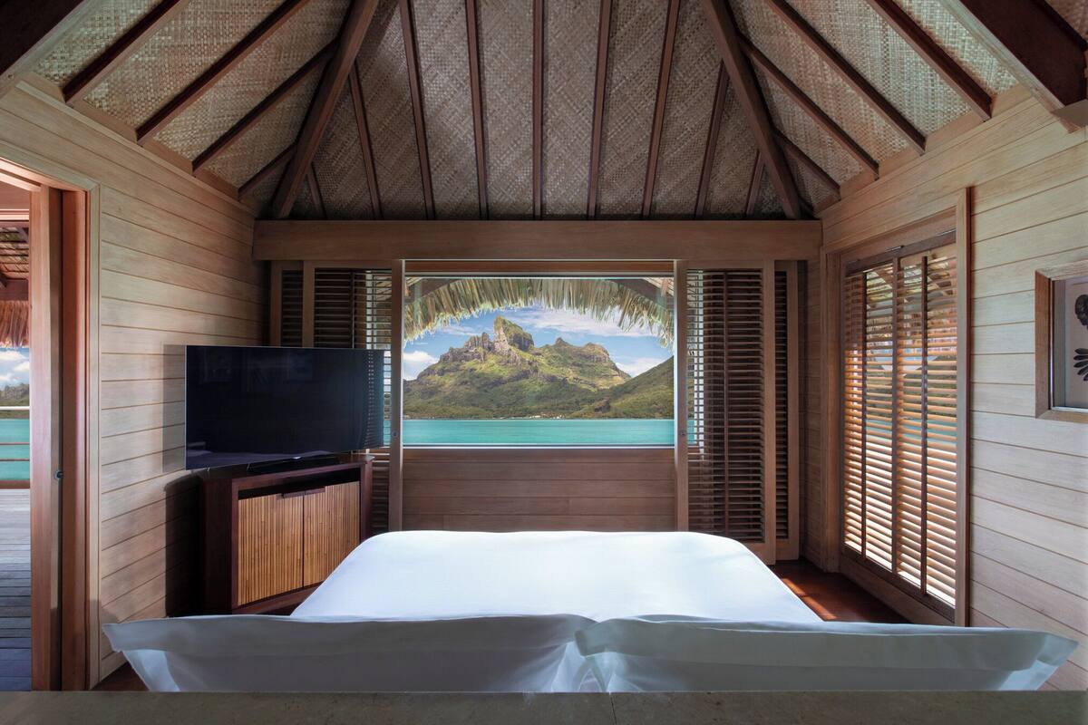 A bedroom with a bed, a television, and a view of a mountainous landscape through a window.