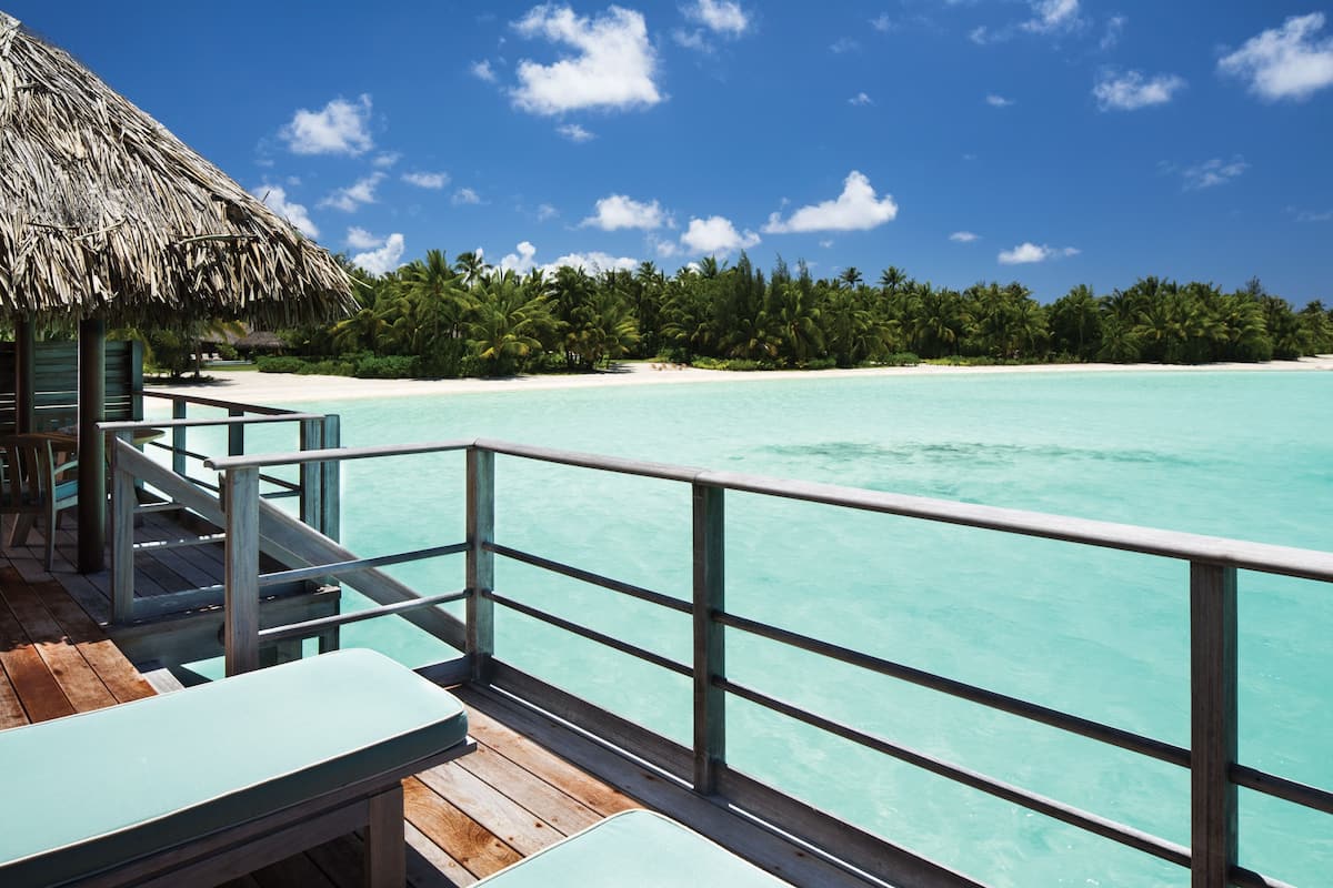 A wooden deck with a railing overlooking turquoise waters and a beach.