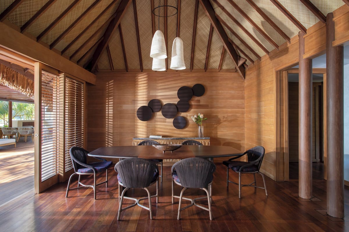 Un comedor con una mesa de madera, cuatro sillas y una lámpara fijada en la pared.