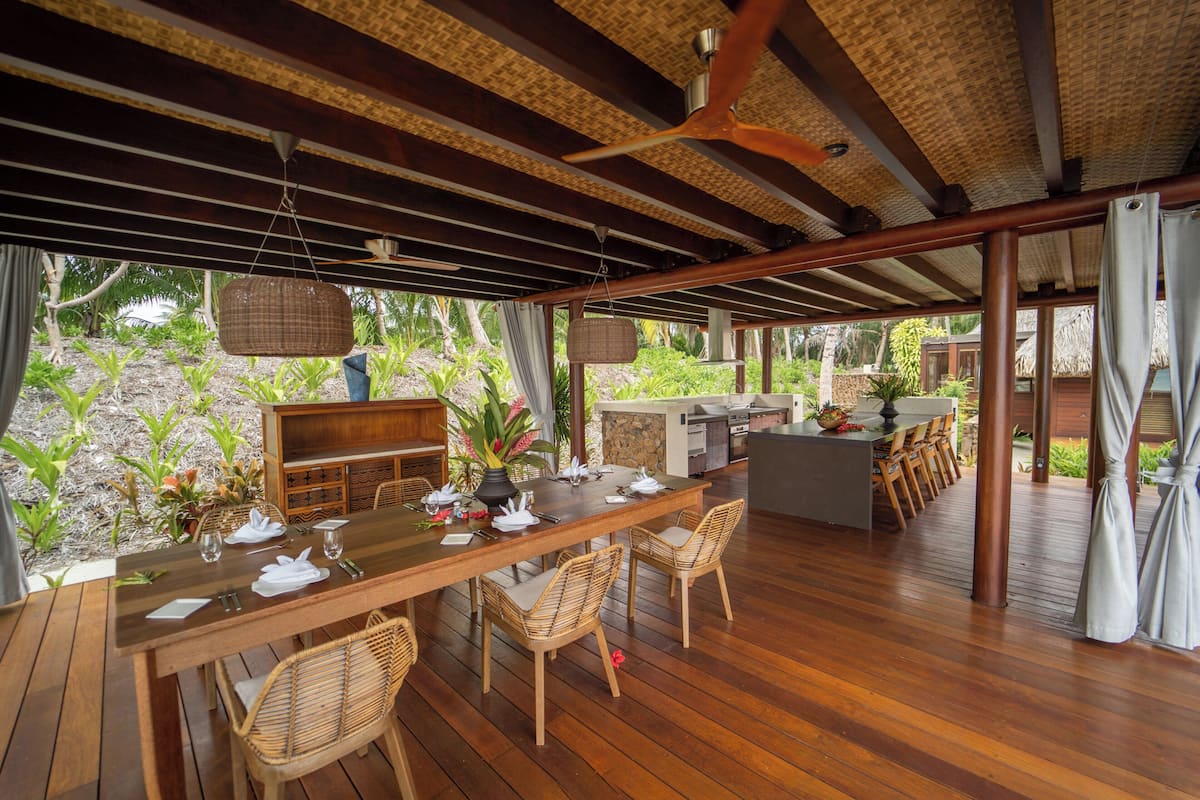 An outdoor dining area with a wooden table, wicker chairs, and a ceiling fan.