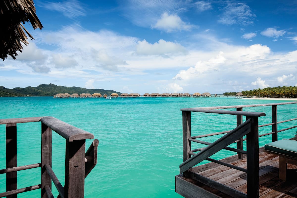 A wooden pier leading to overwater bungalows with turquoise water and clear skies.