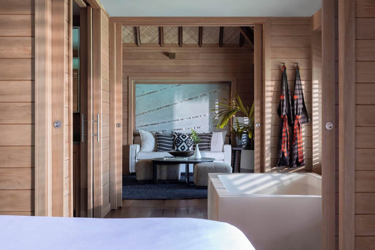 A modern room with a wooden floor, a white sofa, a small table with a plant, and a large mirror on the wall.