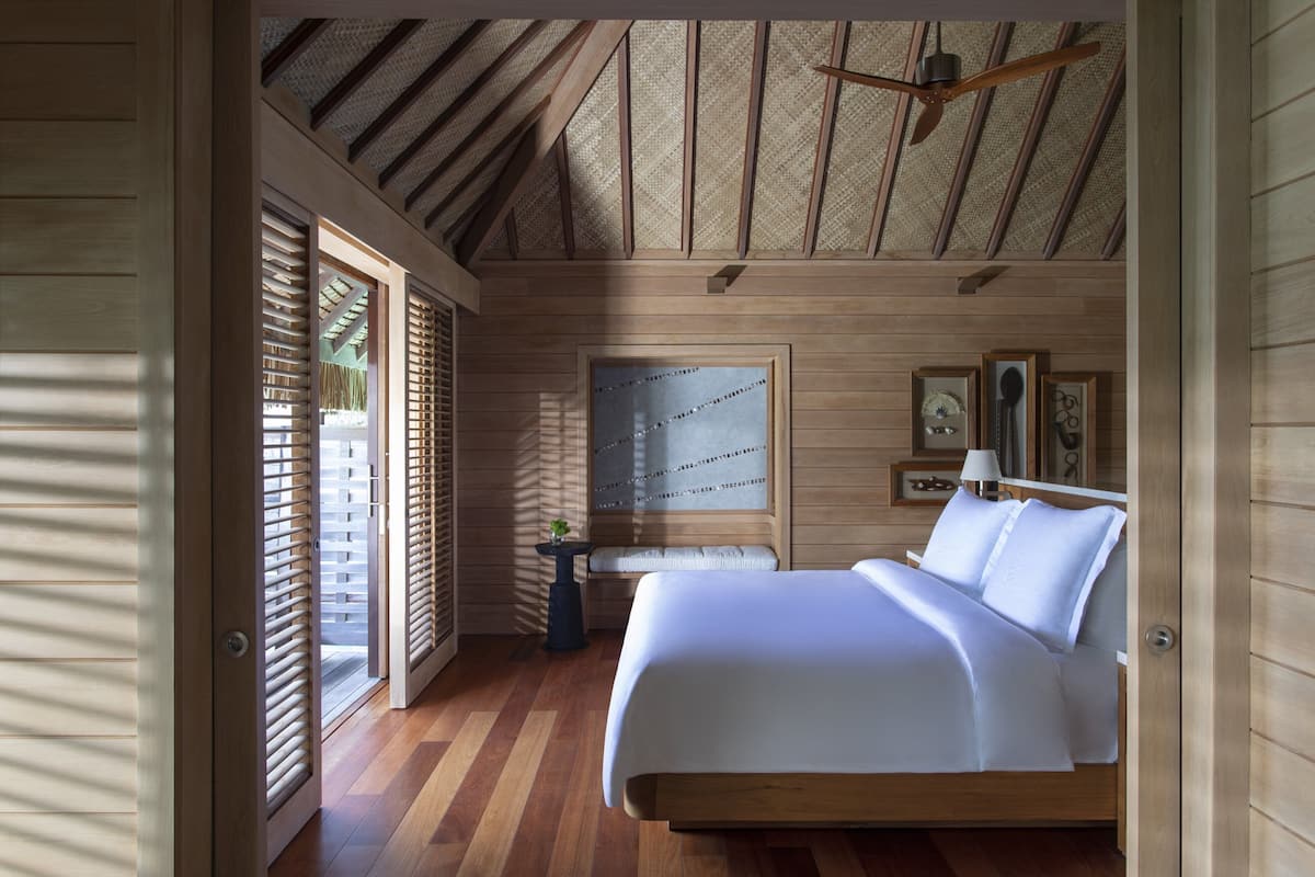 A bedroom with a wooden ceiling, a bed, a nightstand, and a wall-mounted lamp.