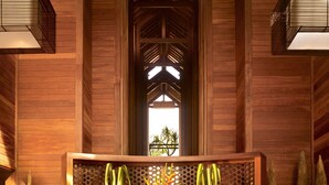 A wooden interior with a central wooden structure, three wooden stands with decorative elements, and a view through a window.