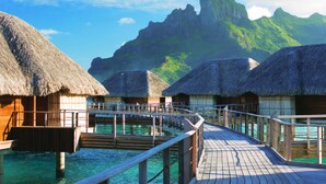 Overwater bungalows with thatched roofs connected by wooden walkways over clear blue water.