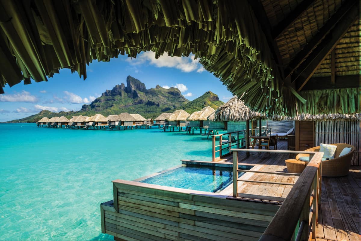 An overwater bungalows with a wooden deck, a pool, and a view of a mountain and ocean.