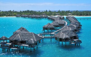 Overwater bungalows with thatched roofs connected by walkways over turquoise waters.