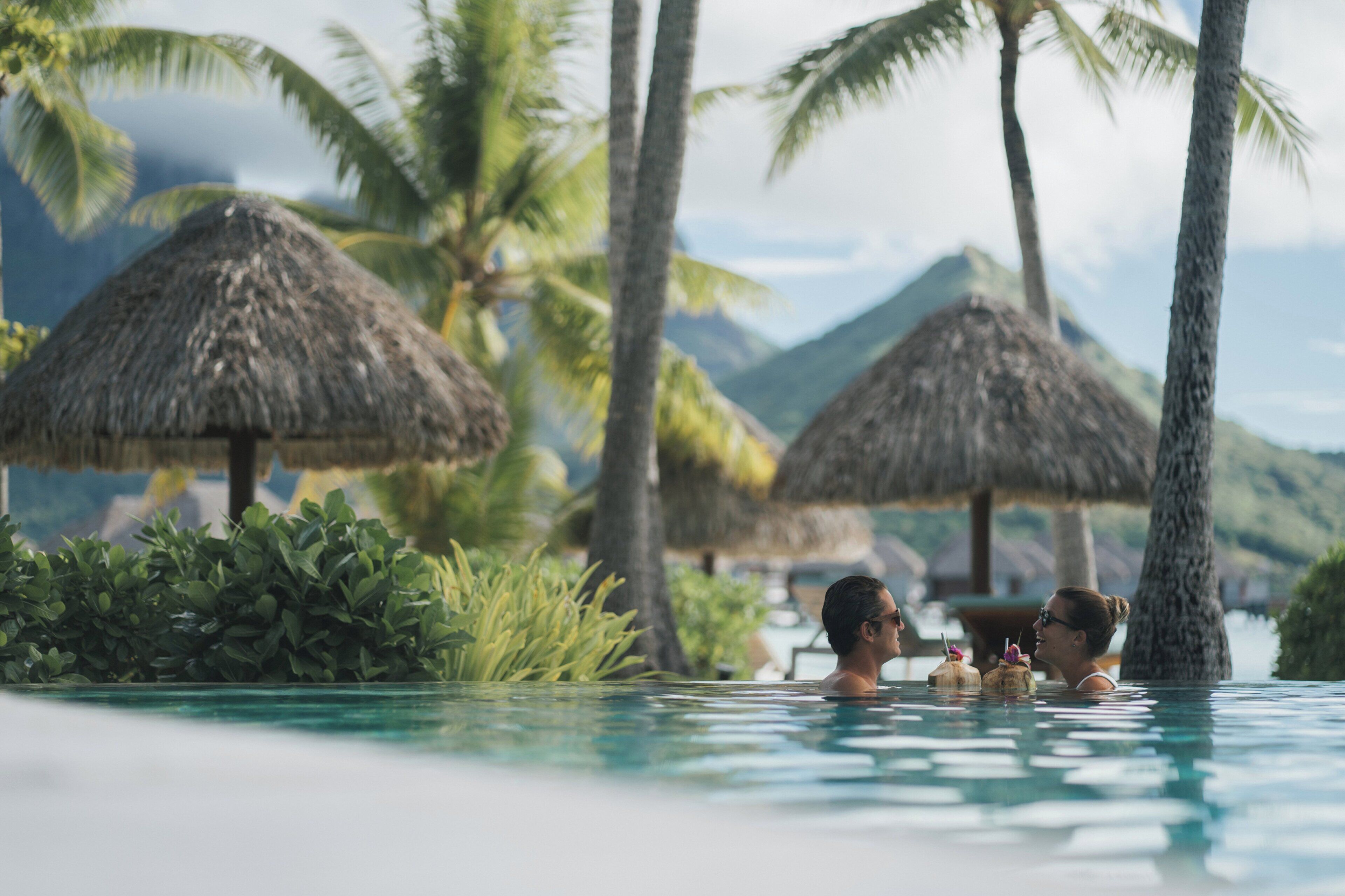 Un área de piscina con sombrillas de paja y palmeras.