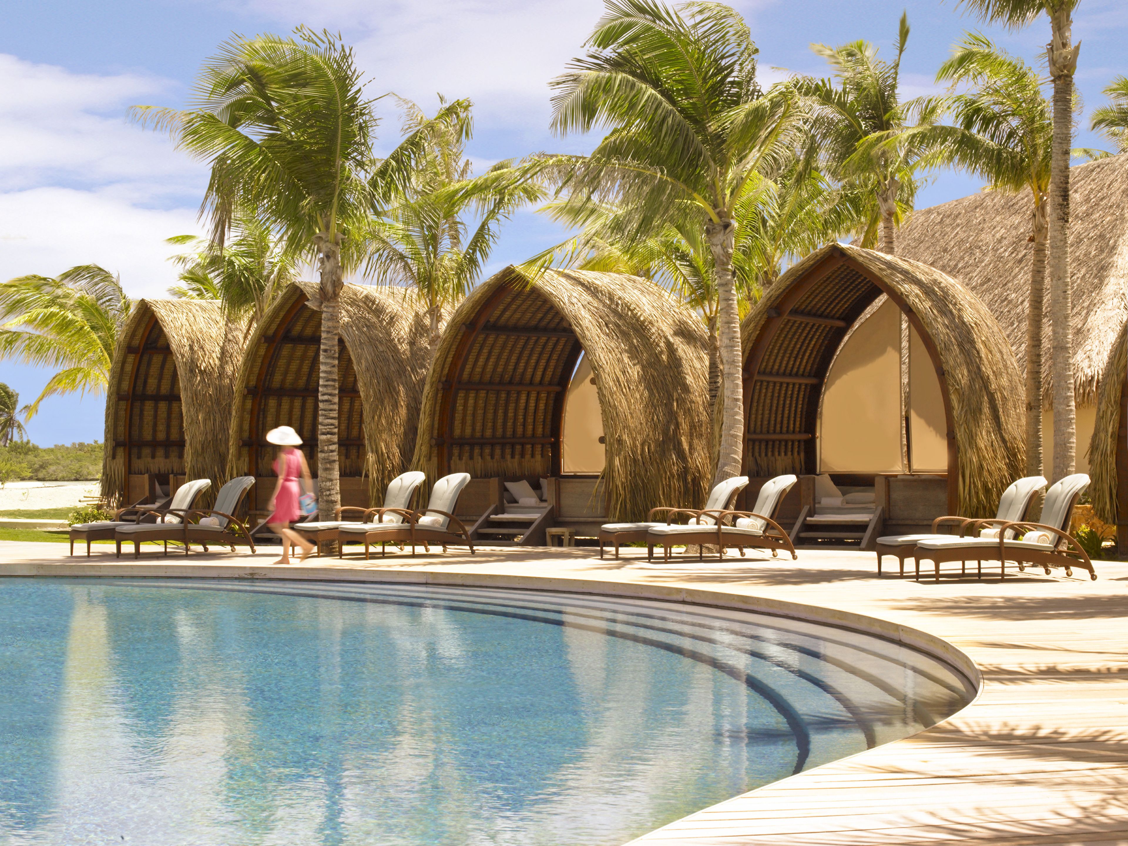 Un espace aménagé au bord de la piscine, avec des chaises longues et des structures dotées de toits en chaume.