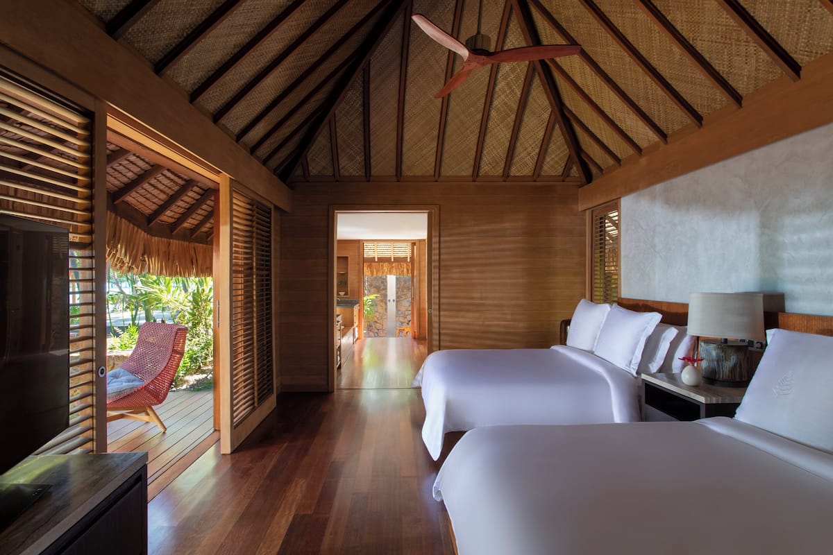 Habitación de hotel con dos camas, televisión, suelo de madera y techo de paja.