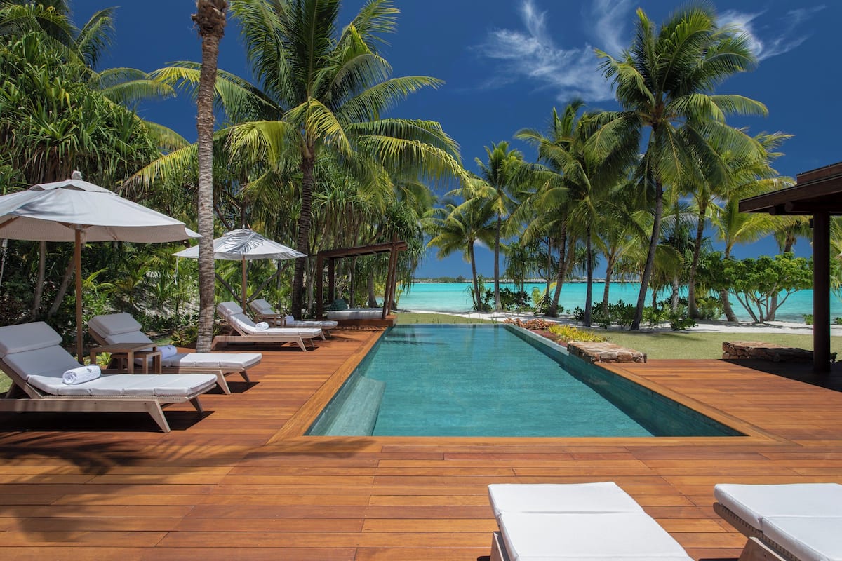 A poolside area with lounge chairs and umbrellas, surrounded by palm trees and a view of the ocean.