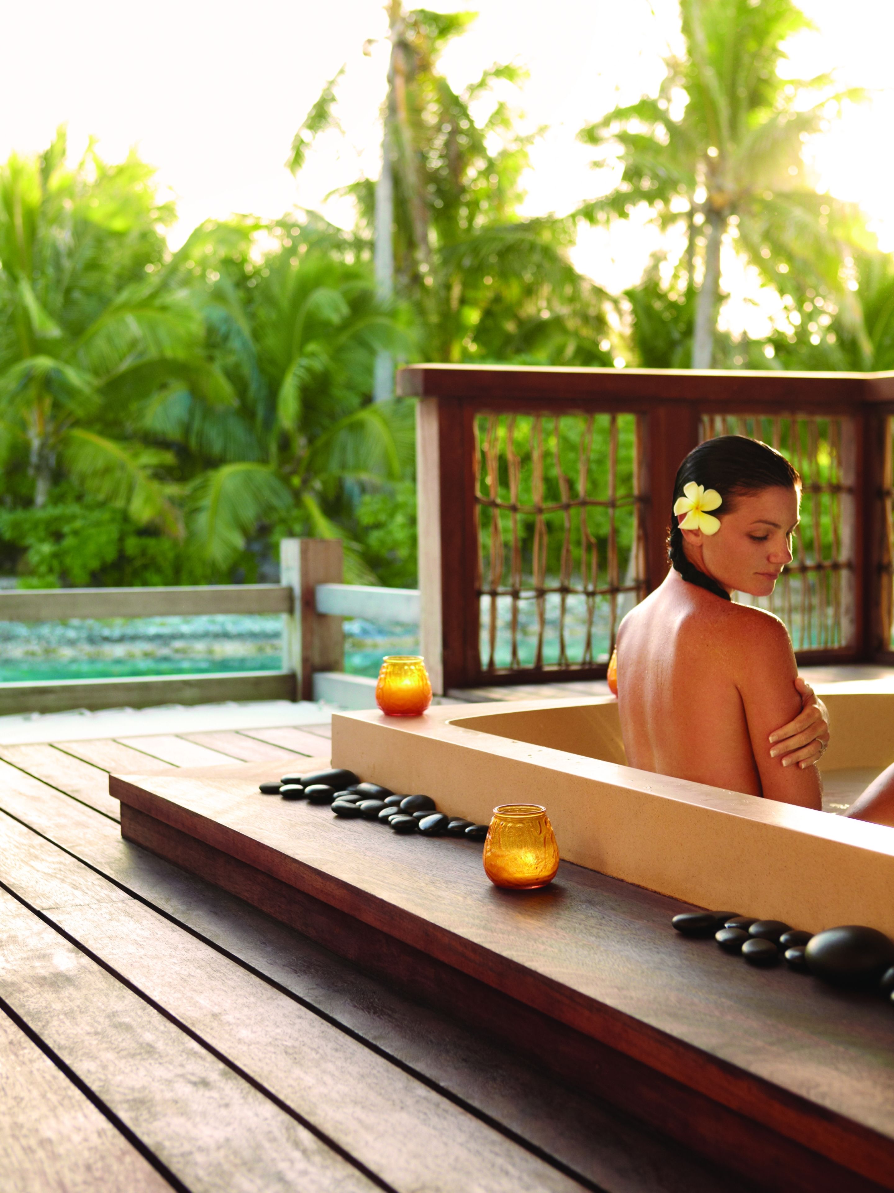 Eine Person in einer Badewanne mit Holzterrasse, zwei Kerzen und schwarzen Steinen.
