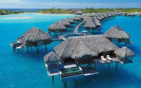 Overwater bungalows with thatched roofs, connected by walkways over clear blue water.