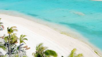 A beach with overwater bungalows, white sand, and palm trees.