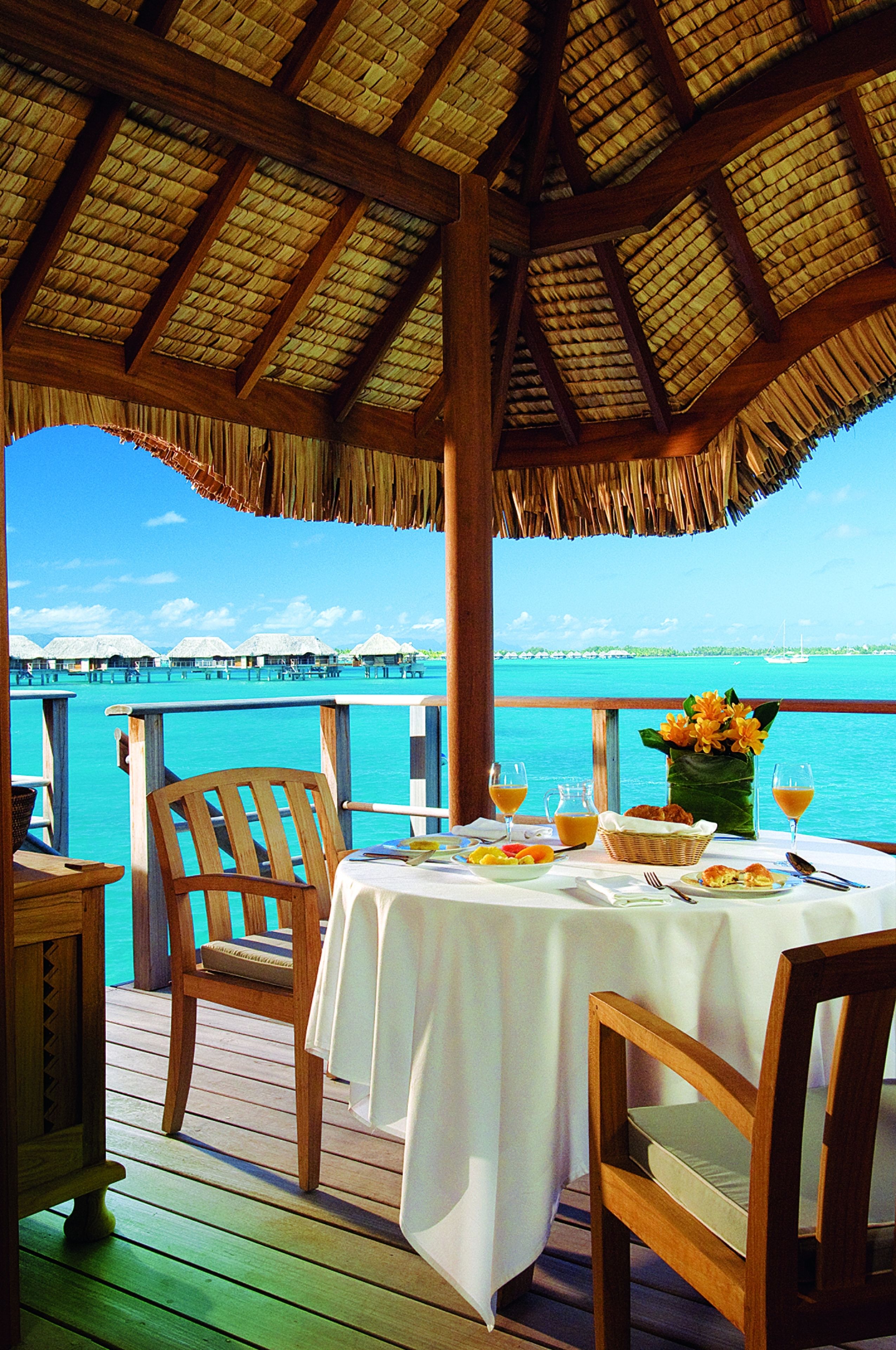 An outdoor dining area with a table set for two, overlooking turquoise waters and a distant island.