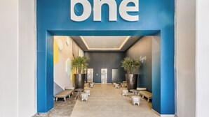 A modern interior with a prominent 'one' sign, seating areas, and large potted plants. - One Acapulco Costera (Acapulco)