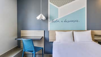 A modern hotel room with a bed, a desk, and a chair.