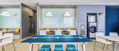 Una sala de reuniones moderna con una mesa larga, taburetes azules y un sofá con cojines amarillos.