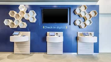 Uma área de recepção com parede azul, uma tela de TV grande e três pias com dispositivos digitais.