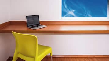 A laptop on a wooden ledge, a bright yellow chair, and a window with a blue sky view.
