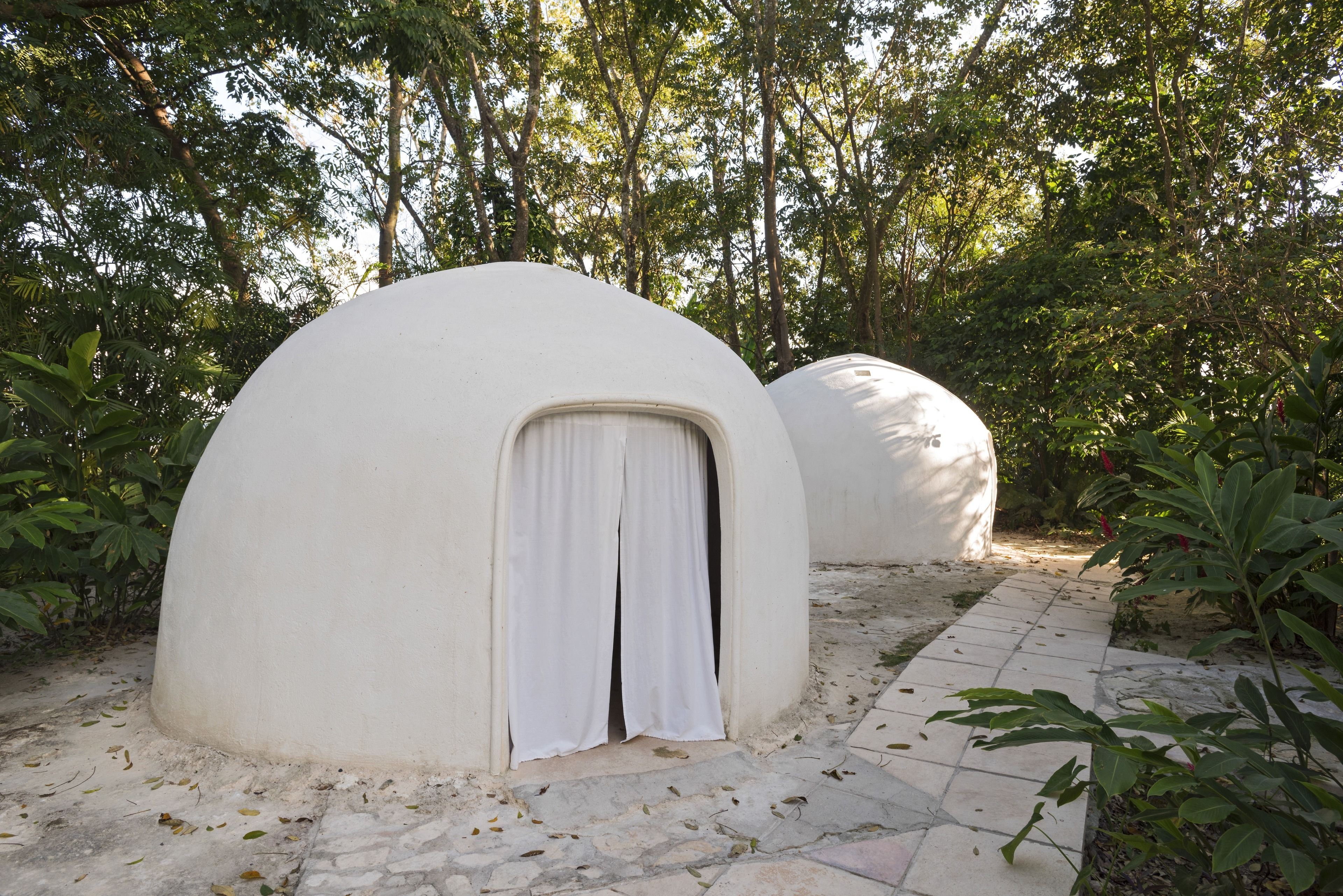 Deux structures en forme de dôme, dotées d’une petite entrée et d’un rideau, entourées de verdure et bordées d’un chemin de pierre.
