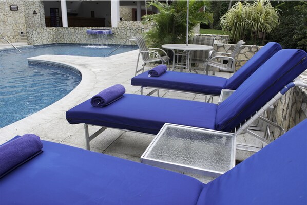 A poolside area with lounge chairs and a small table, surrounded by stone walls and greenery. - Hotel Camino Real Tikal (San Jose Peten)