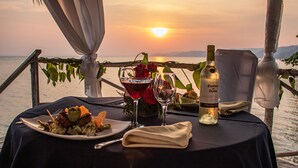 Une table dressée pour un repas, avec une bouteille de Casillero del Diablo, un plat de nourriture et un verre de vin rouge, donnant sur un coucher de soleil.