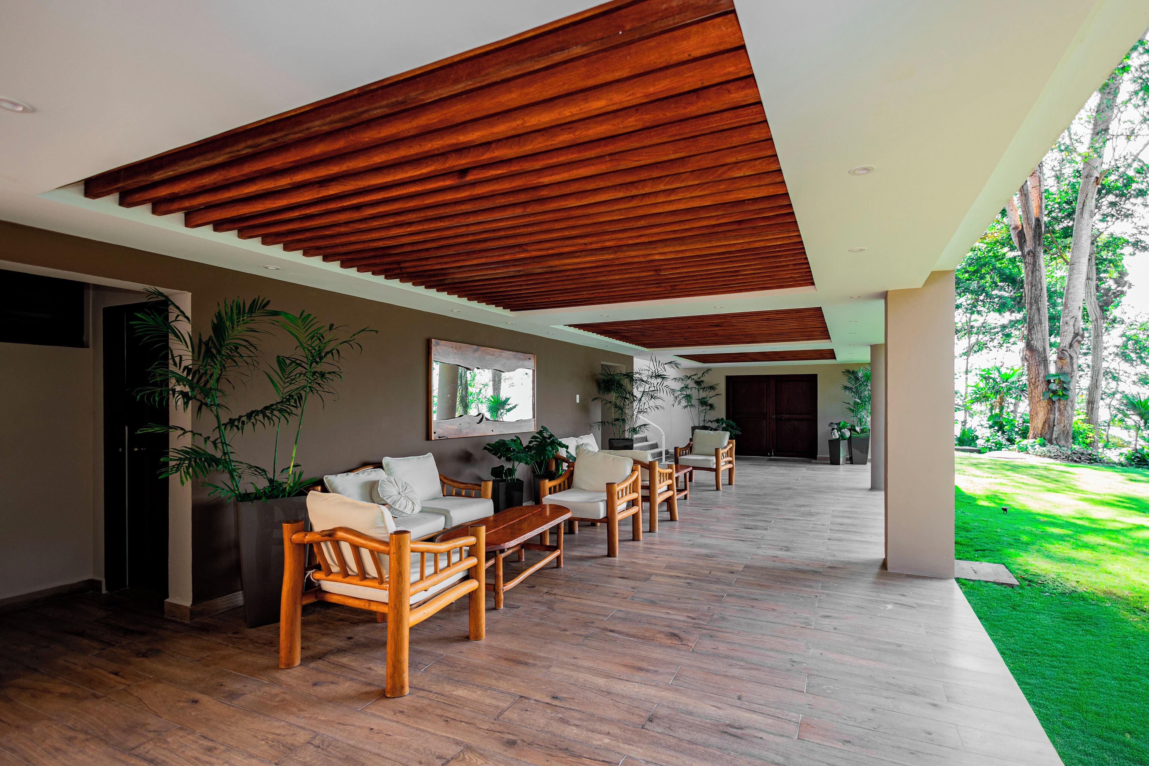 A spacious indoor area with wooden flooring, a long dining table, multiple chairs, and potted plants.
