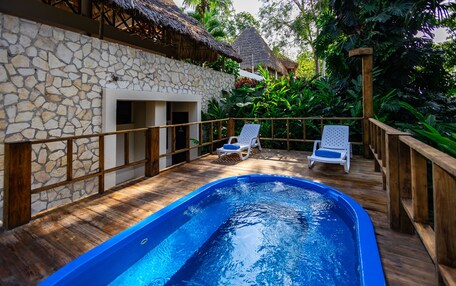 A swimming pool with wooden deck and lounge chairs, surrounded by stone walls and tropical vegetation.
