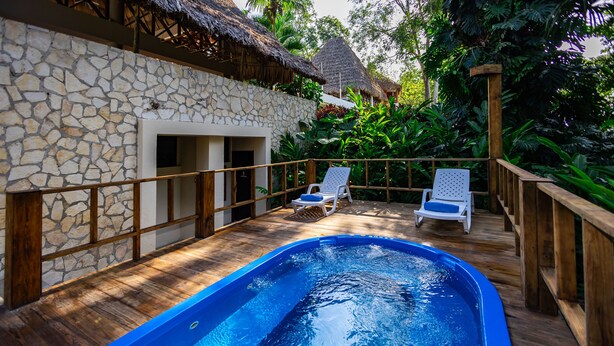Une piscine dotée d’une terrasse en bois et de chaises longues, entourée de murs en pierre et d’une végétation tropicale.