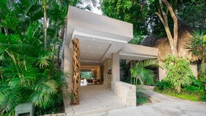 Un bâtiment moderne doté d’une façade en pierre, d’un toit de chaume et d’une végétation tropicale luxuriante.