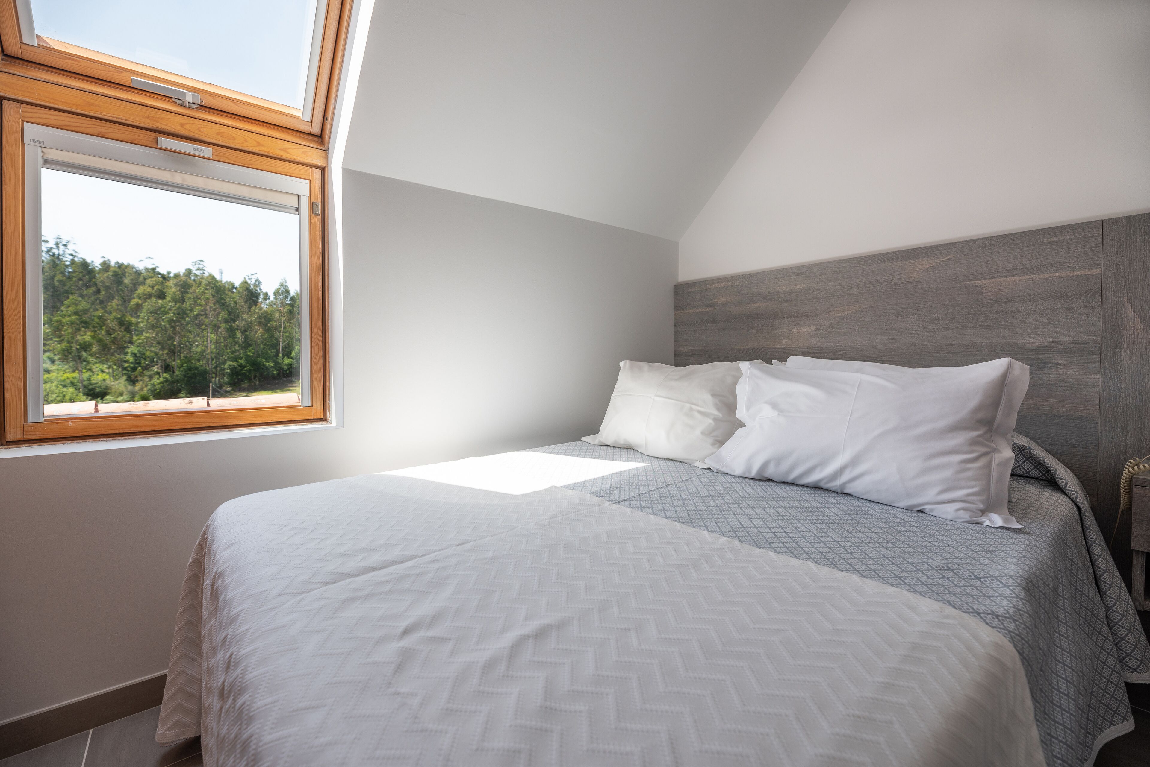 A bedroom with a large window, a bed with white bedding, and a wooden headboard.