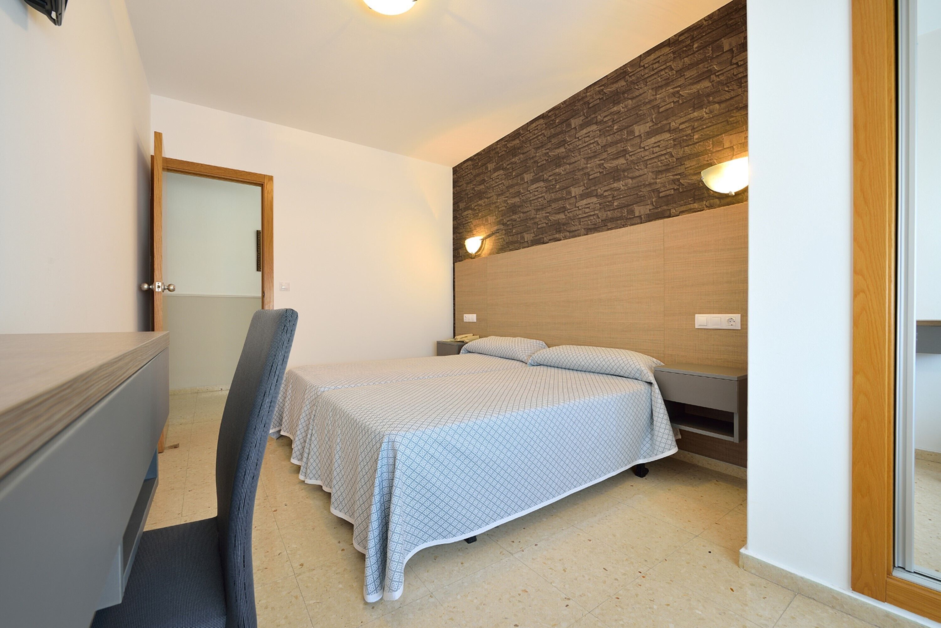 A bedroom with a bed, a desk, and a chair.