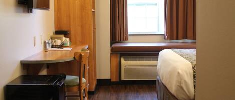 A compact hotel room with a kitchenette, a bed, a window with curtains, and a built-in heater.