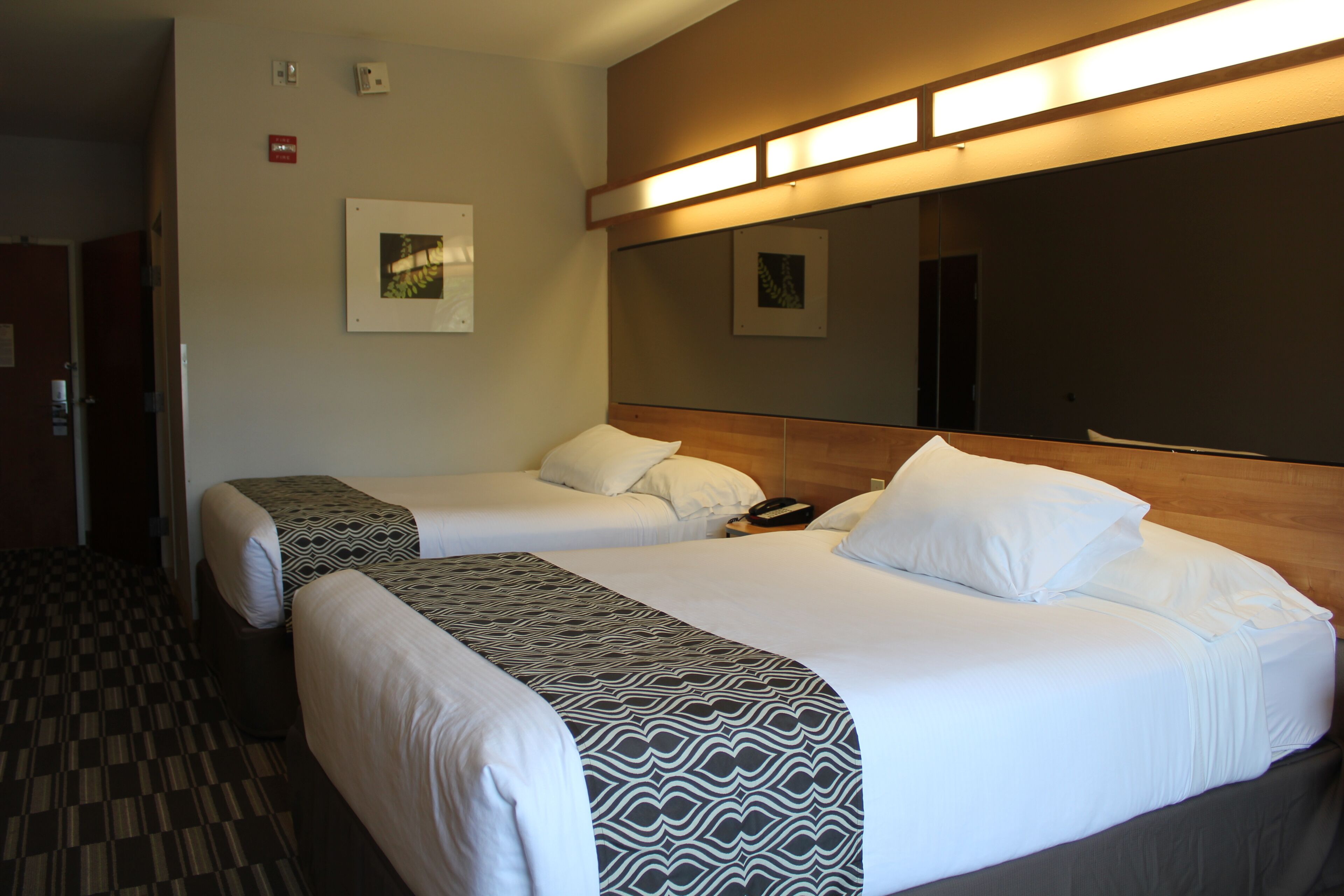 Habitación de hotel con dos camas, una colcha estampada, cabecera de madera y una lámpara fijada a la pared.