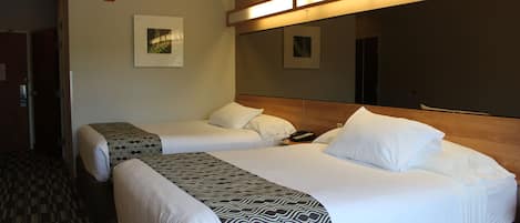 Habitación de hotel con dos camas, una colcha estampada, cabecera de madera y una lámpara fijada a la pared.