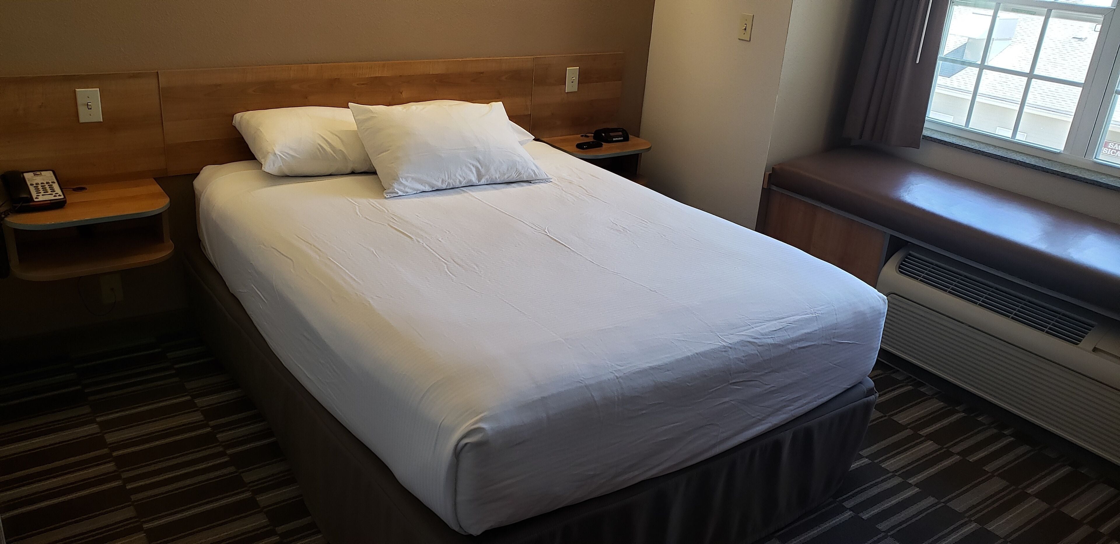 A hotel room with a large bed, two bedside tables, a telephone, and a window with a view.