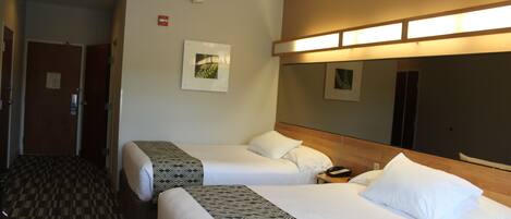 A hotel room with two beds, a wooden headboard, a bedside table with a phone, and a carpeted floor.