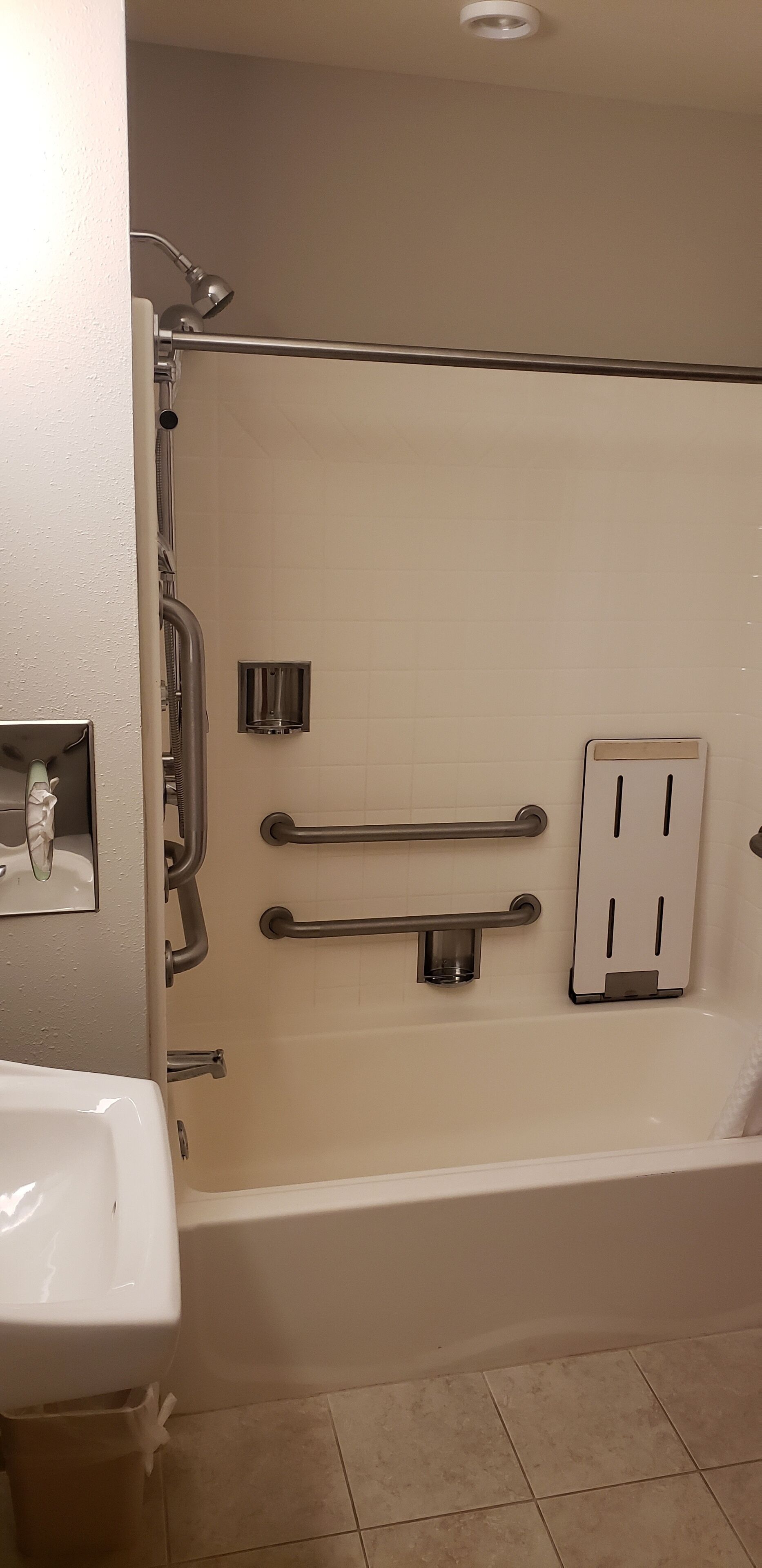 A bathroom with a bathtub, a sink, and a shower. There are grab bars and a hand dryer.