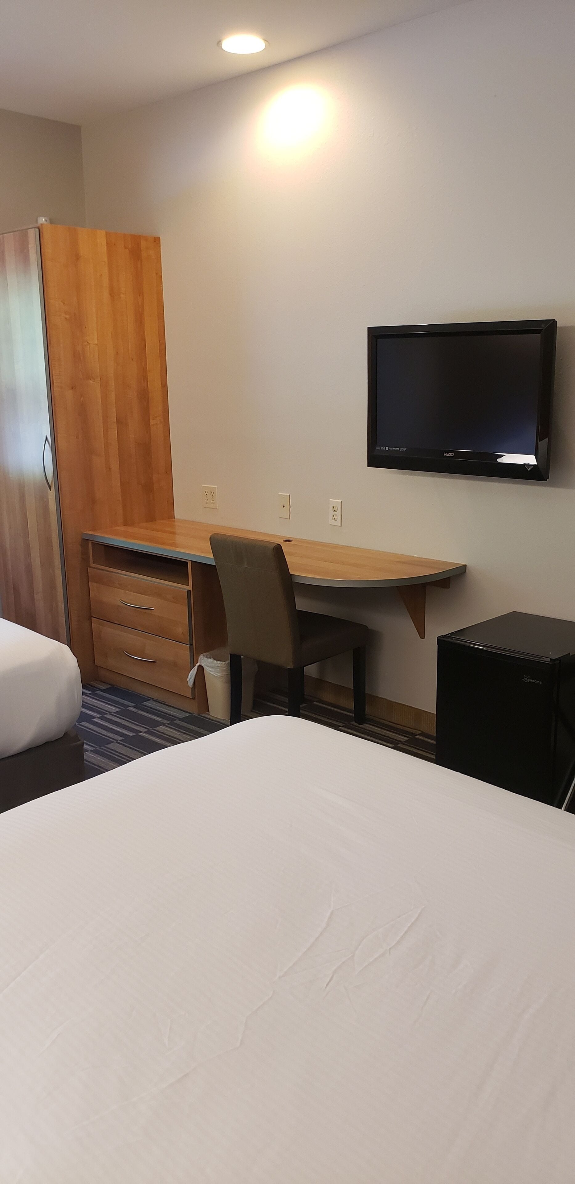 A hotel room with a bed, a desk, a chair, a television, and a wardrobe.