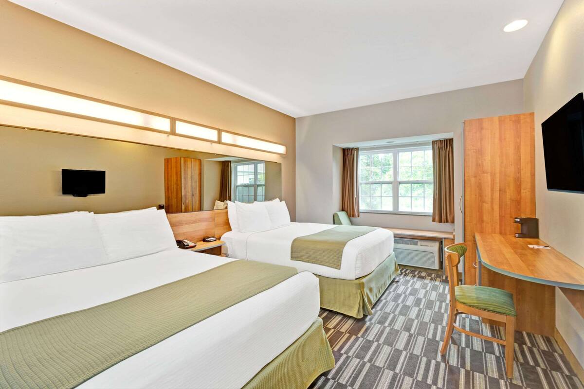 A hotel room with two beds, a desk, a chair, a TV, and a window with curtains.
