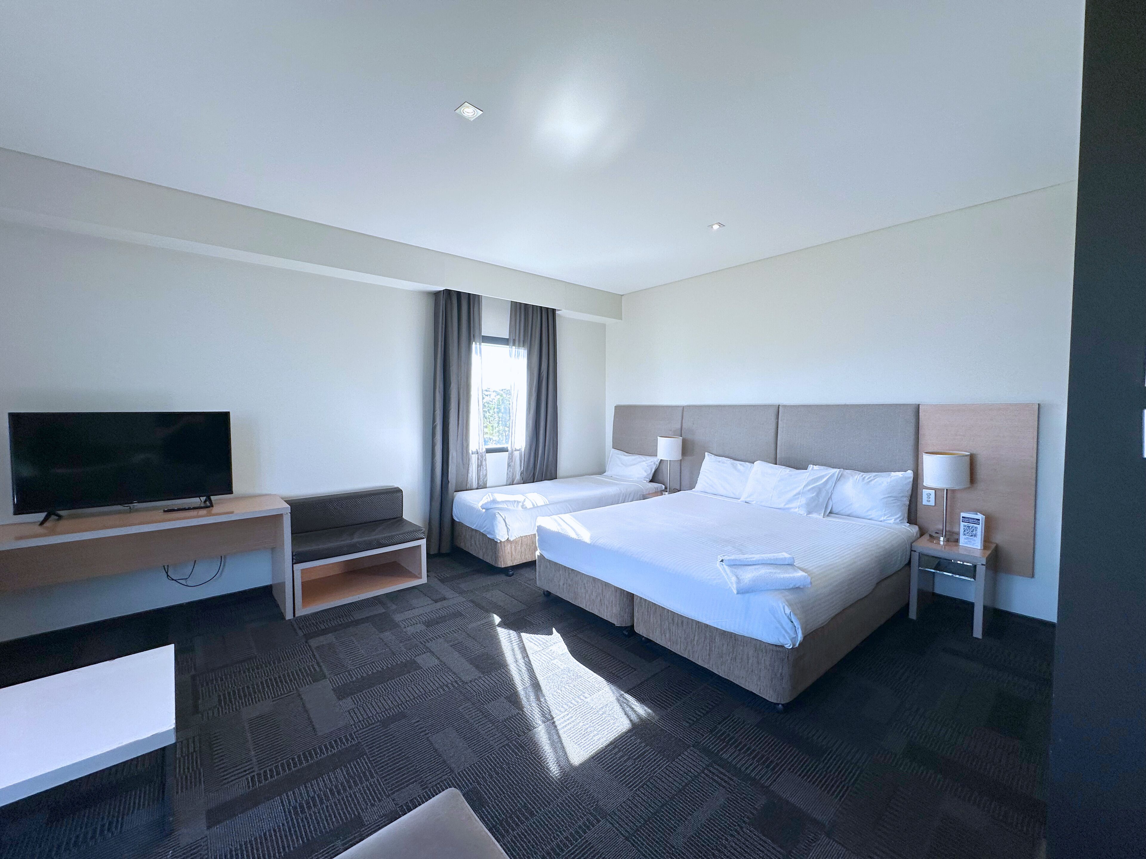 A hotel room with two beds, a TV, a desk, and a window with curtains.